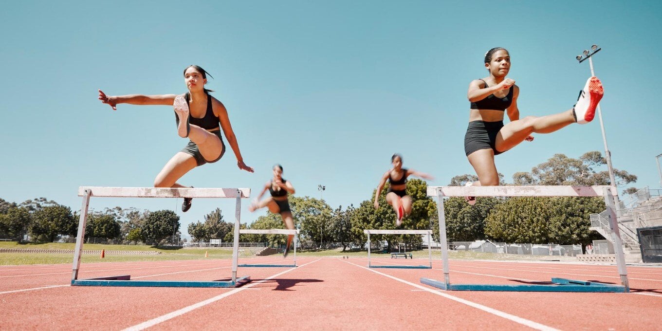 girls running track jumping hurdles